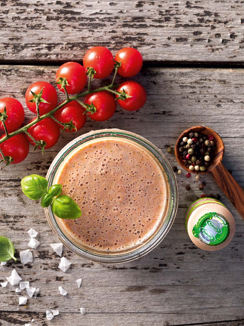 Smoothie met komkommer, tomaatjes, basilicum, houten lepel met peperkorrels, flesje Yakult Plus.