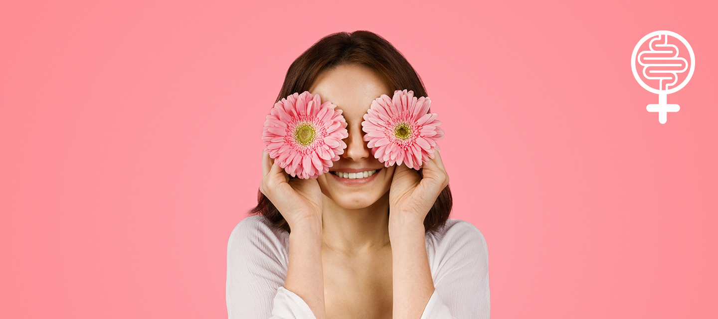 Cheerful young caucasian woman with a playful expression covering her eyes with two pink gerbera flower