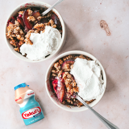 Yakult Balance flesje met twee schaaltjes gevuld met een ovengegrilde appel-bessencrumble en een kaneelcrème en in ieder schaaltje een lepel.